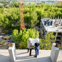 Top view on the construction site of residential buildings on the green area with two workers looking on the construction process